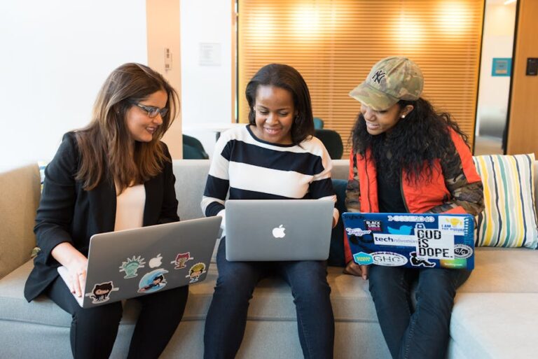 Three women working together on laptops in a casual office setting, emphasizing teamwork and collaboration.