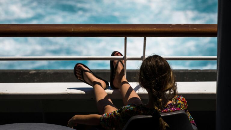 Woman relaxing on a cruise ship deck, looking at the ocean in summer.