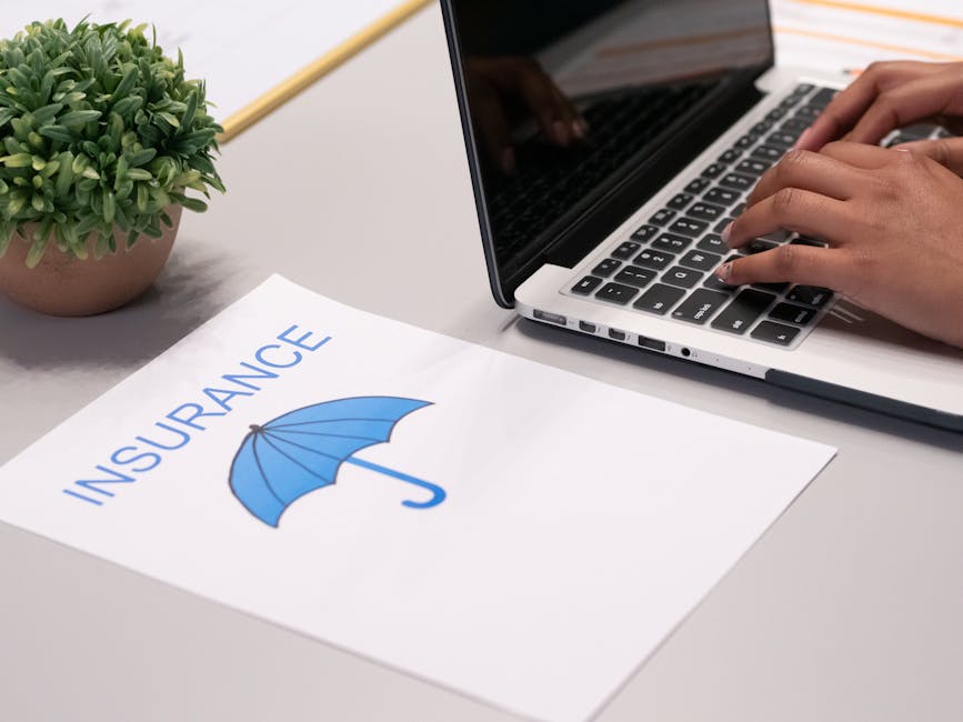 Close-up of hands typing on laptop with an insurance document visible on the desk.